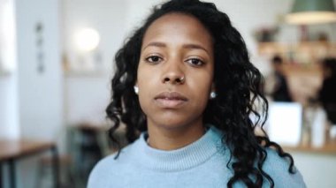 Mavi kazak giyen, konsantre olmuş esmer Afrikalı kadın kafedeki kameraya bakıyor.