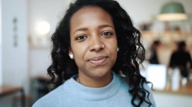 Kahkaha atan esmer Afrikalı kadın mavi kazak giyip kafede kameraya bakıyor.