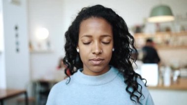 Kahvede mavi kazak giyen mutlu esmer kadın kameraya gözlerini açıyor.