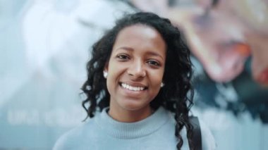 Kahkaha atan esmer Afrikalı kadın mavi kazak giyip açık havada kameraya bakıyor.