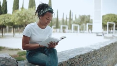 Pleased brunette African woman reading book outdoors