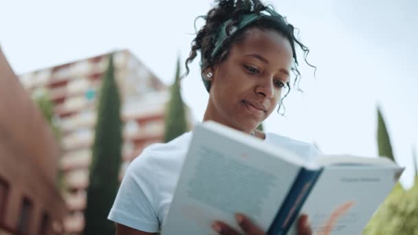 Positive Brunette African Woman Reading Book Outdoors — стоковое видео