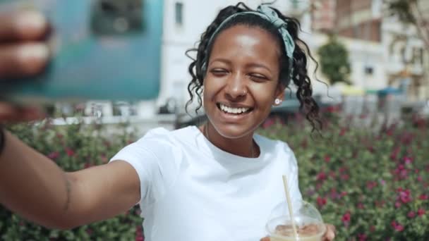 陽気なブルネットアフリカの女性録画ビデオと飲み物ジュース屋外 — ストック動画