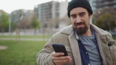 Gülen sakallı adam, dışarıda telefonla konuşurken şapkasını takıyor.