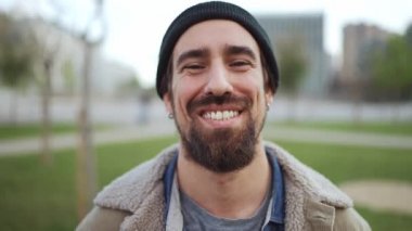 Şapka takan neşeli sakallı adam kameraya dışarıda bakıyor.