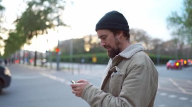 Şehirde cep telefonuyla yazan şapkalı dalgın sakallı bir adam.