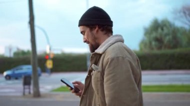 Şapka takan yakışıklı bir adam şehirde geziyor ve cep telefonuyla yazıyor.
