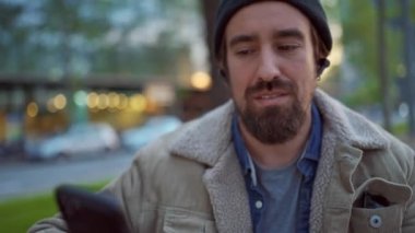 Şapka takan yakışıklı bir adam şehirde dans ediyor ve telefona bakıyor.