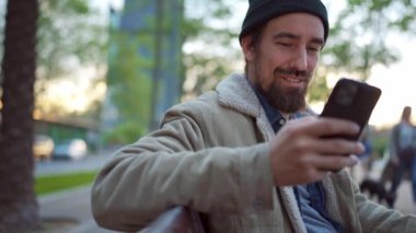 Şehirde telefonla mesajlaşan şapkalı olumlu bir adam.