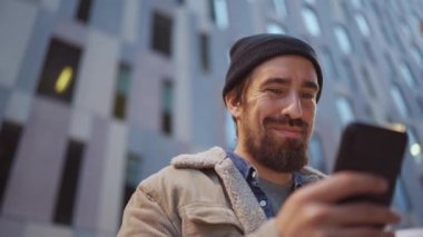 Gülümseyen adam cep telefonuyla yazarken ve dışarıda kahve içerken