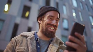 Dışarıdaki telefonlara binaları gösteren şapkalı gülen adam.