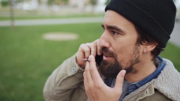 Серьезный Бородатый Мужчина Шляпе Разговаривает Телефону Курит Открытом Воздухе — стоковое видео