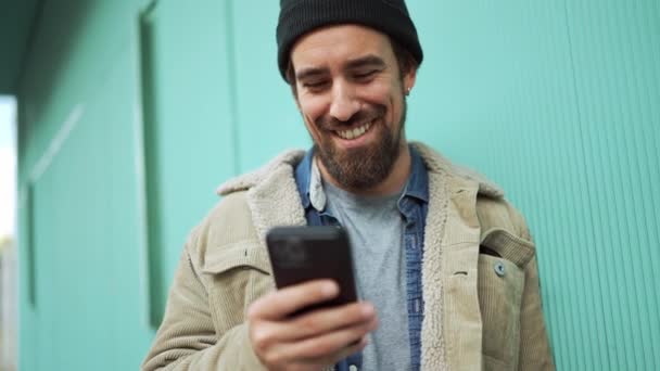 Positiv Skäggig Man Klädd Hatt Skriva Telefon Och Prata Utomhus — Stockvideo