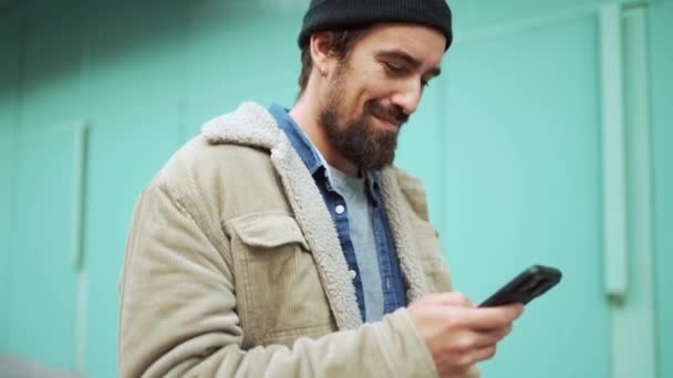 快乐的大胡子男人 戴着帽子 电话发短信 走在户外 — 图库视频影像