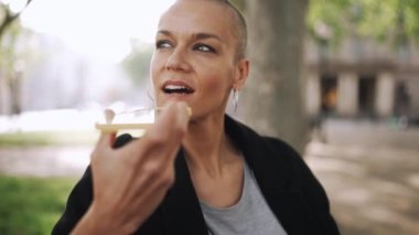 Parktaki bankta telefonla sesli mesaj kaydeden kel bir kadın.