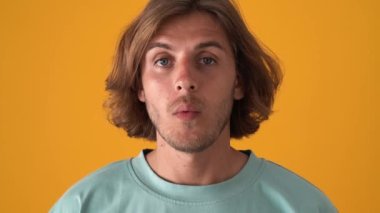 Şaşkın sarışın adam sarı stüdyodaki kameraya bakıyor.