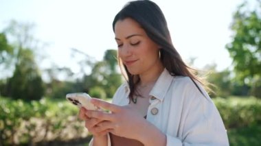 Pozitif esmer kadın cep telefonuna bakıyor ve dışarıda yürüyor.