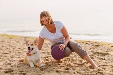 Yaşlı kadın köpeğiyle kumsalda dinlenirken gülümsüyor.