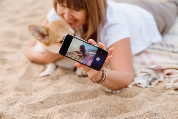 Son sınıf öğrencisi, kumsalda köpeğiyle dinlenirken cep telefonuyla fotoğraf çekiyor.