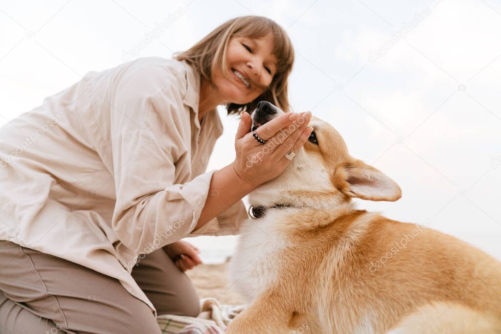 Senior woman smiling while resting with her dog on sandy beach