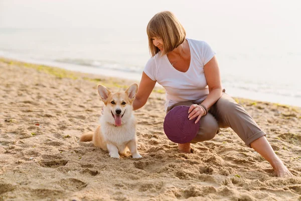 Yaşlı kadın köpeğiyle kumsalda dinlenirken gülümsüyor.