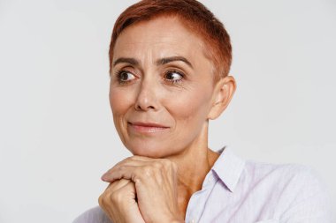 Kızıl saçlı, kısa saçlı, gülümseyen ve beyaz arka planda tek başına kalan yaşlı bir kadın.