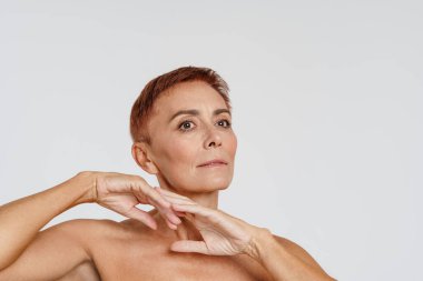 Üstsüz, kısa saçlı yaşlı bir kadın. Beyaz arka planda izole edilmiş bir şekilde bekliyor.