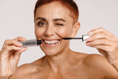 Beyaz arka planda, kısa saçlı, maskara gösteren son sınıf üstsüz kadın.