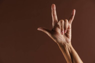Kahverengi duvardan izole edilmiş kamerada boynuz hareketi gösteren yaşlı bir kadın.