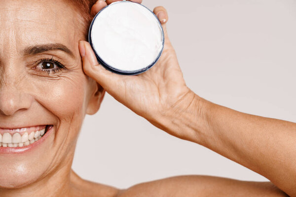 Senior shirtless woman with short hair showing face cream isolated over white background