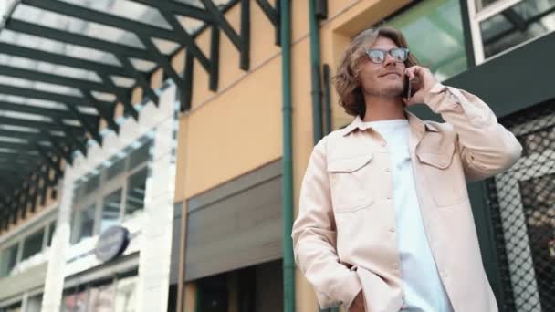 携帯電話屋外で話している眼鏡のハンサムなブロンド男 — ストック動画