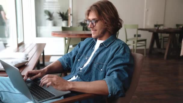 Kahkahalar Atan Gözlüklü Sarışın Adam Kafede Dizüstü Bilgisayarda Yazı Yazıyor — Stok video