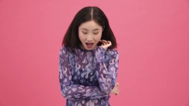 Gülümseyen Asyalı kadın pembe stüdyoyu işaret ediyor.