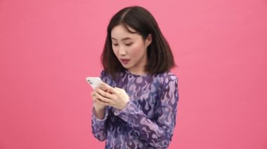 Yakışıklı Asyalı kadın pembe stüdyoda telefonla selfie çekiyor.