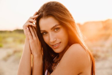 Kumsalda gülümseyen ve kameraya bakan genç esmer kadın.