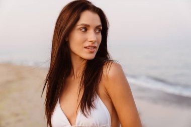 Genç esmer kadın poz veriyor ve kumsala bakıyor.