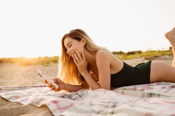 Young Blonde Woman Smiling Using Cellphone While Lying Beach — Stock Photo, Image