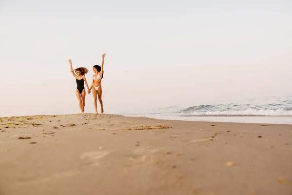 Молоді Білі Жінки Посміхаються Тримаються Руки Під Час Бігу Пляжі — стокове фото