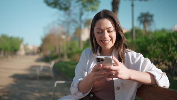 Mulher Morena Feliz Digitando Celular Enquanto Sentada Banco — Vídeo de Stock