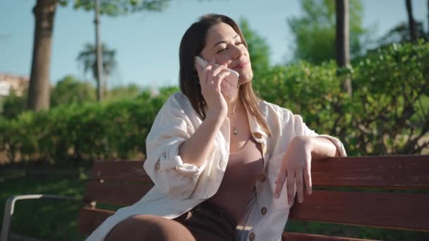 一个英俊的黑发女人坐在长椅上 一边用手机聊天 — 图库视频影像
