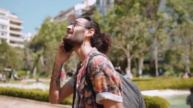 Gülümseyen kıvırcık saçlı, gözlüklü, dışarıda telefonla konuşan adam.