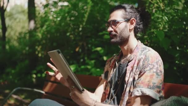Dışardaki Bankta Otururken Tablete Bakan Gözlüklü Kıvırcık Saçlı Sakallı Adam — Stok video