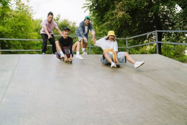 Çok ırklı gençler dışarıda kaykay parkında vakit geçirirken eğleniyorlar.