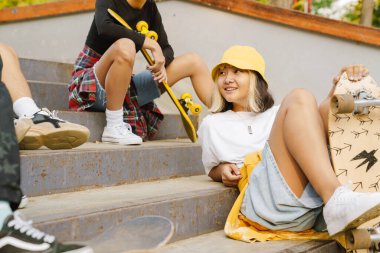 Yaz günü kaykay parkında dinlenirken gülümseyen ve konuşan çok ırklı arkadaşlar.