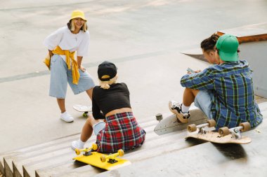 Yaz günü kaykay parkında dinlenirken gülümseyen ve konuşan çok ırklı arkadaşlar.