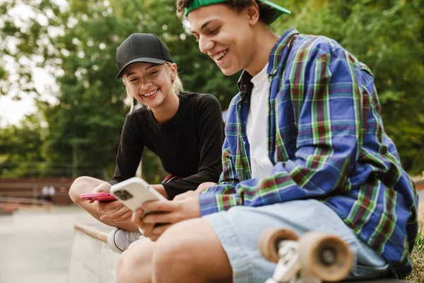 Dos Adolescentes Multirraciales Sonriendo Usando Teléfonos Celulares Mientras Pasan Tiempo —  Fotos de Stock