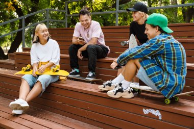 Kaykay parkında zaman geçirirken konuşan ve gülen çok ırklı gençler.