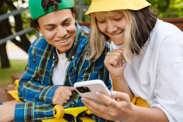Två Multiraciala Tonåringar Ler Och Använder Mobiltelefon Medan Tillbringar Tid — Stockfoto