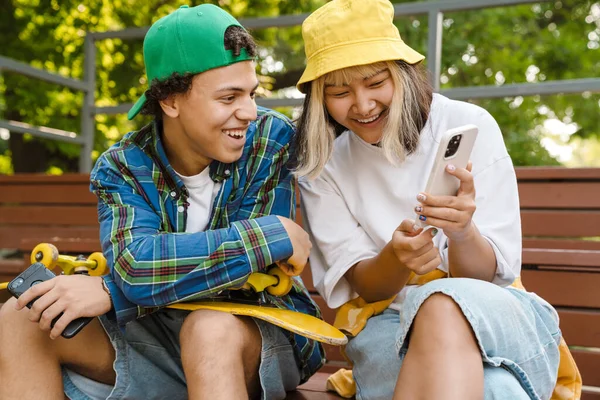 Två Multiraciala Tonåringar Ler Och Använder Mobiltelefon Medan Tillbringar Tid — Stockfoto