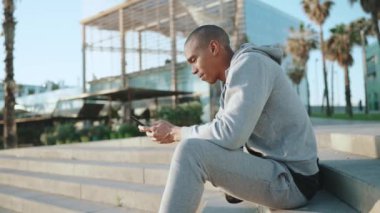 Neşeli kel sporcu sabah dışarıda otururken telefonla mesaj atıyor.